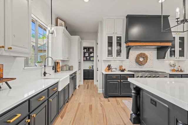 kitchen featuring light countertops, a sink, white cabinets, decorative light fixtures, and light wood-style floors