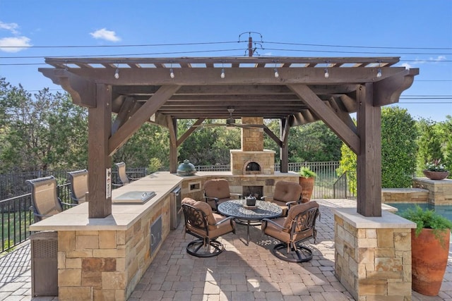 view of patio / terrace with a gazebo, an outdoor kitchen, an outdoor stone fireplace, and fence