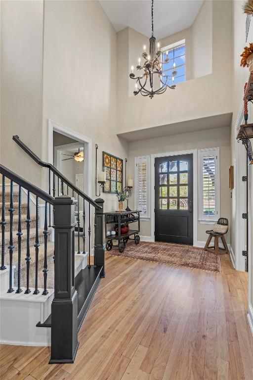 entrance foyer featuring ceiling fan with notable chandelier, baseboards, stairs, and wood finished floors