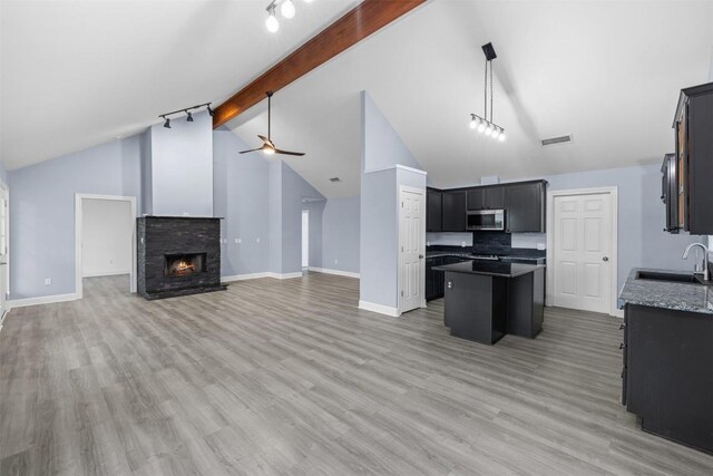 kitchen featuring stainless steel microwave, a kitchen island, a sink, beam ceiling, and visible vents