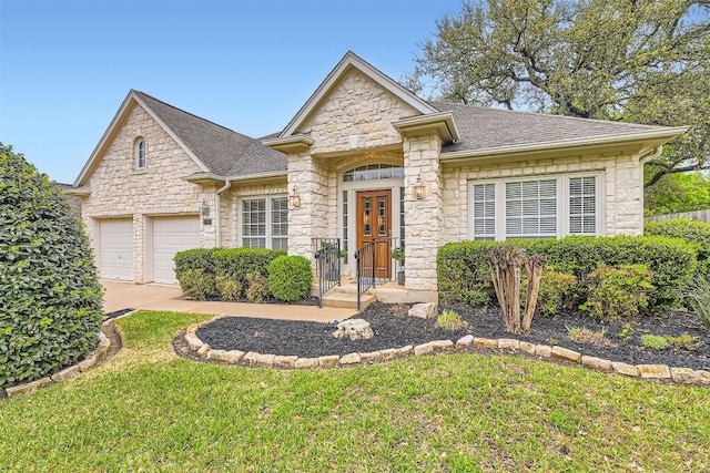view of front of house with driveway, stone siding, an attached garage, a front lawn, and a shingled roof