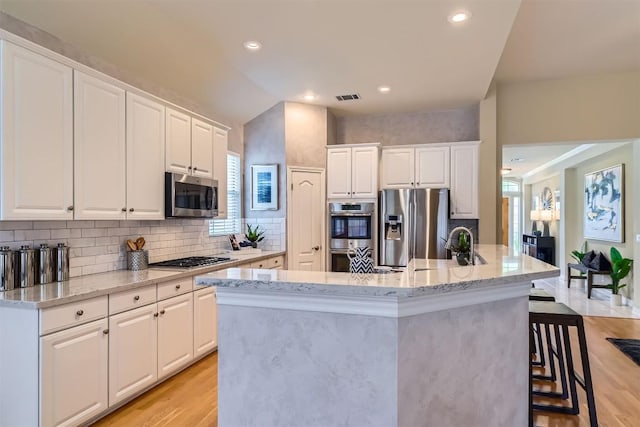 kitchen with an island with sink, visible vents, light wood-style floors, and stainless steel appliances