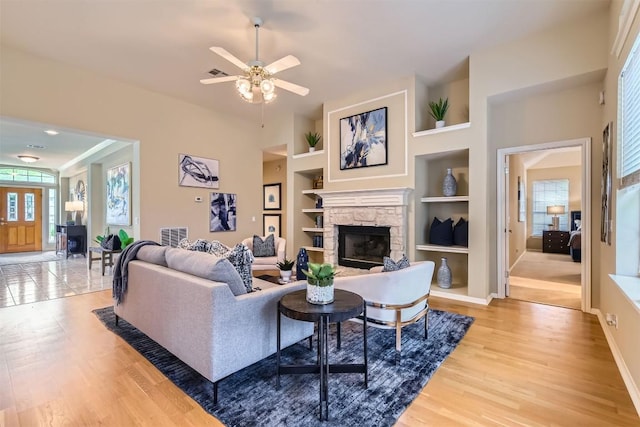 11100 Comiso Pala Path, Austin, TX 78726 - living room featuring a stone fireplace, built in shelves, light wood-style flooring, and a ceiling fan