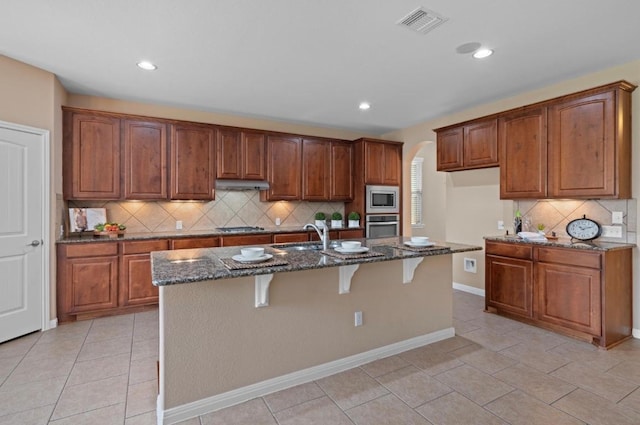 17920 Silent Harbor Loop, Pflugerville, TX 78660 - kitchen with appliances with stainless steel finishes, under cabinet range hood, dark stone countertops, tasteful backsplash, and arched walkways