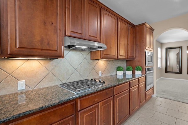 17920 Silent Harbor Loop, Pflugerville, TX 78660 - kitchen with under cabinet range hood, stainless steel appliances, arched walkways, decorative backsplash, and dark stone countertops