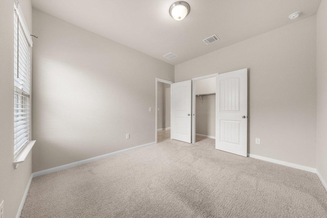 unfurnished bedroom with baseboards, visible vents, a closet, and light carpet