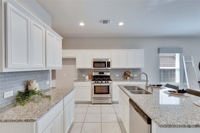 kitchen featuring a sink, backsplash, appliances with stainless steel finishes, light tile patterned floors, and white cabinets