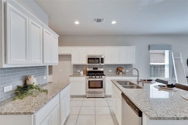 6608 May Shower Dr, Austin, TX 78744 - kitchen featuring appliances with stainless steel finishes, tasteful backsplash, white cabinetry, light tile patterned floors, and a center island with sink