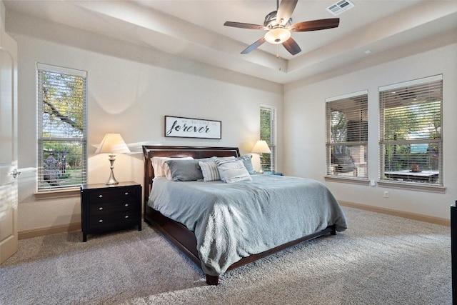 carpeted bedroom with baseboards, a tray ceiling, visible vents, and a ceiling fan