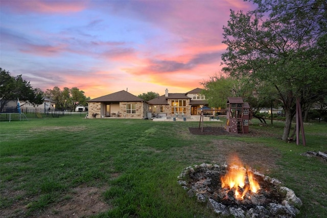 view of yard featuring a trampoline, an outdoor fire pit, fence, a patio, and a playground