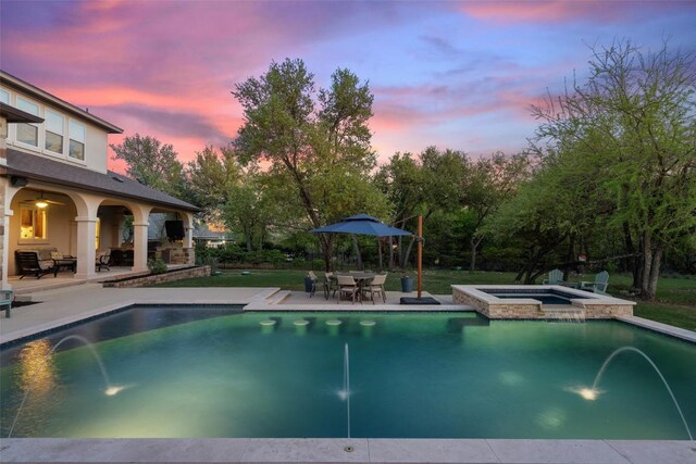 pool at dusk with a pool with connected hot tub and a patio area