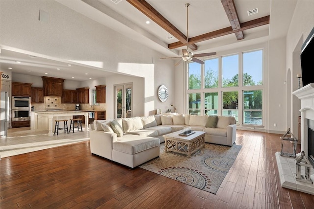 living room featuring beamed ceiling, a fireplace with raised hearth, a high ceiling, and light wood-type flooring