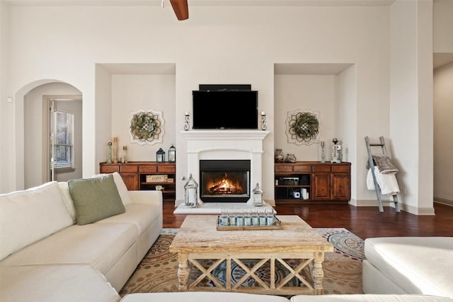 living area featuring dark wood-type flooring, a lit fireplace, arched walkways, and baseboards