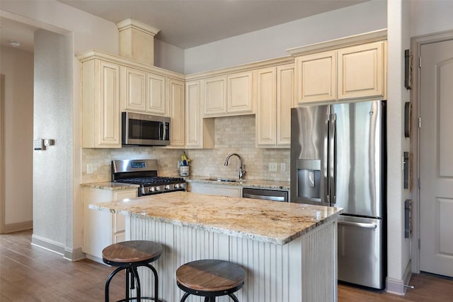 kitchen with decorative backsplash, light stone countertops, appliances with stainless steel finishes, a sink, and cream cabinets