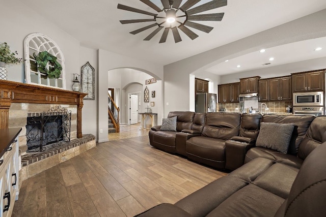 living area featuring recessed lighting, a fireplace with raised hearth, arched walkways, light wood-style floors, and a ceiling fan