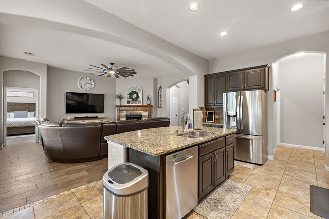 kitchen with ceiling fan, appliances with stainless steel finishes, arched walkways, a sink, and light stone counters