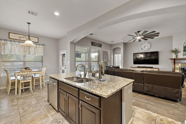 kitchen with stainless steel dishwasher, a sink, arched walkways, ceiling fan, and light stone countertops