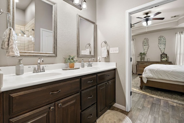 ensuite bathroom featuring double vanity, a sink, a ceiling fan, and wood finished floors