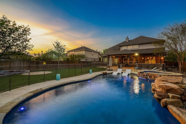 pool at dusk featuring a lawn, a fenced in pool, a fenced backyard, and a patio area