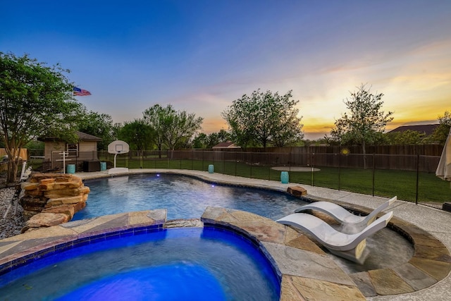 pool at dusk with cooling unit, an outbuilding, fence, a pool with connected hot tub, and a lawn