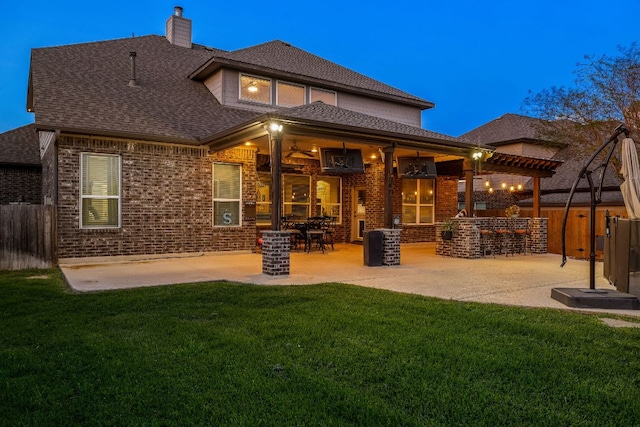 rear view of house featuring a patio area, roof with shingles, fence, brick siding, and a lawn