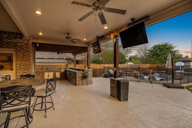 view of patio / terrace featuring fence, exterior kitchen, outdoor dining space, and a ceiling fan