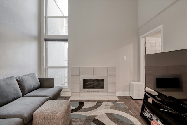 living room featuring a towering ceiling, baseboards, wood finished floors, and a tile fireplace