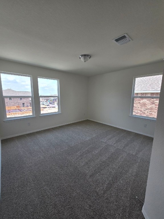 empty room featuring visible vents, plenty of natural light, and dark colored carpet