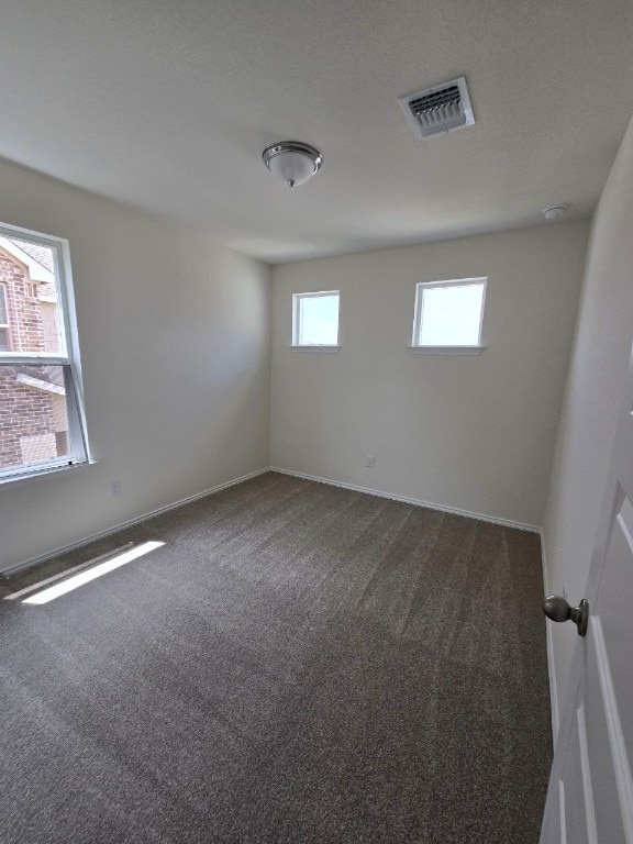 spare room with baseboards, dark colored carpet, and visible vents