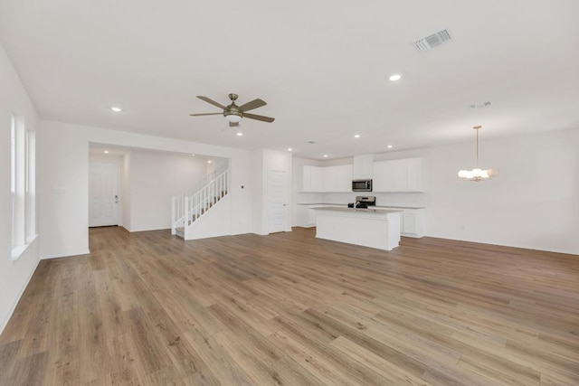4915 Mozzafiato Ln, Round Rock, TX 78665 - unfurnished living room featuring a ceiling fan, stairway, light wood-type flooring, a chandelier, and recessed lighting