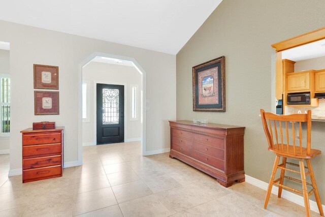 foyer featuring light tile patterned floors, arched walkways, baseboards, and lofted ceiling