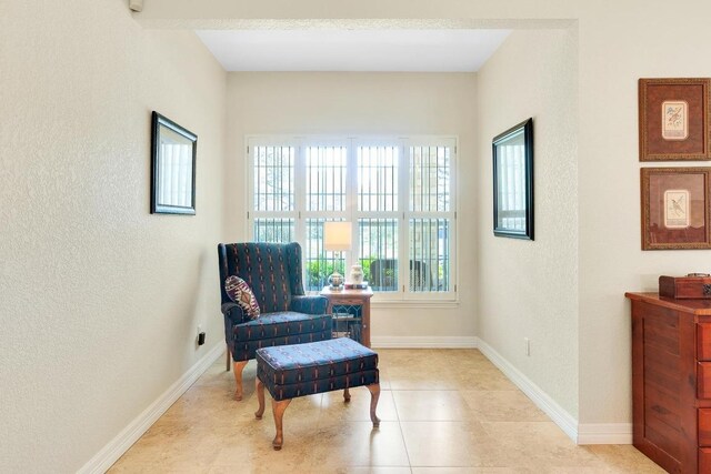 living area with baseboards, a textured wall, and light tile patterned floors