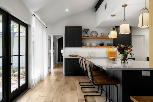 10100 Dobbin Dr, Austin, TX 78748 - kitchen featuring backsplash, vaulted ceiling, open shelves, dark cabinets, and light wood-type flooring