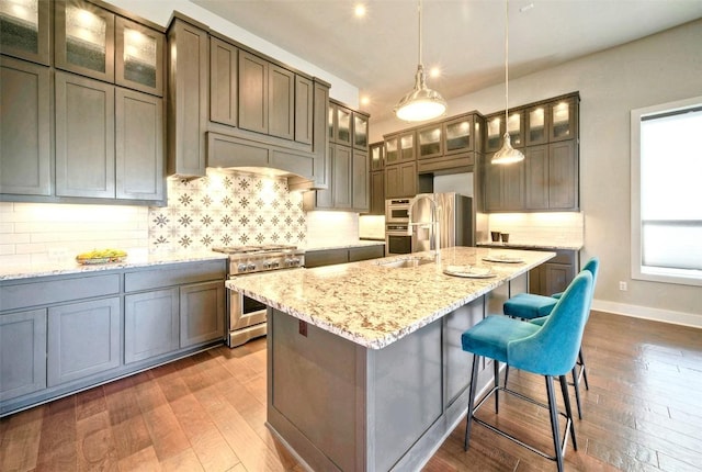 12113 Beautybrush Dr, Austin, TX 78738 - kitchen with stainless steel appliances, dark wood-style floors, tasteful backsplash, light stone counters, and a kitchen bar