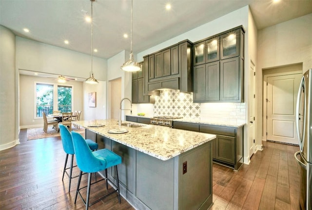 12113 Beautybrush Dr, Austin, TX 78738 - kitchen featuring stainless steel fridge, an island with sink, light stone countertops, dark wood-style flooring, and recessed lighting