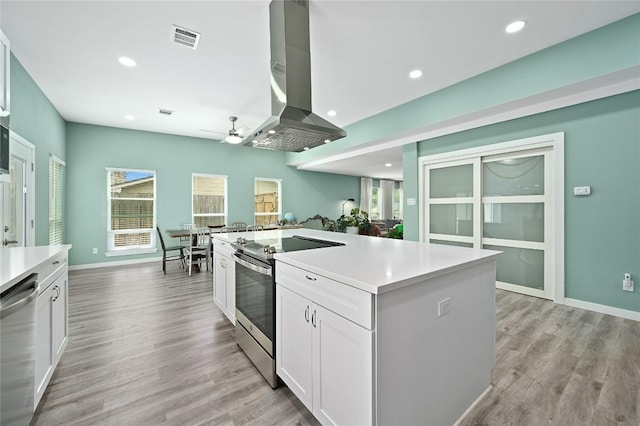 kitchen with ceiling fan, wall chimney range hood, light countertops, white cabinets, and appliances with stainless steel finishes