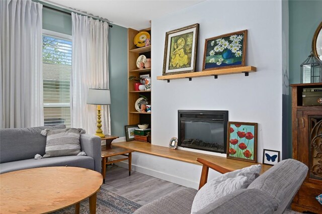living room with a glass covered fireplace, baseboards, built in features, and wood finished floors