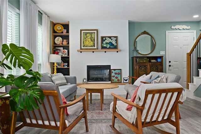 living area with built in features, a glass covered fireplace, wood finished floors, and stairway