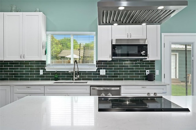 kitchen with appliances with stainless steel finishes, range hood, a sink, light countertops, and white cabinetry