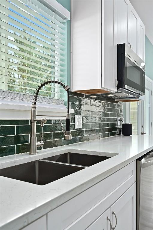 kitchen with white cabinets, stainless steel appliances, decorative backsplash, and a sink