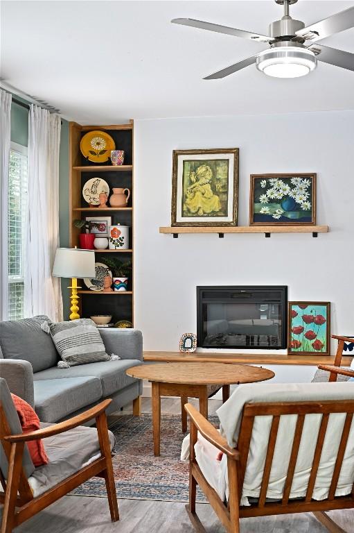 living area with built in features, ceiling fan, and wood finished floors