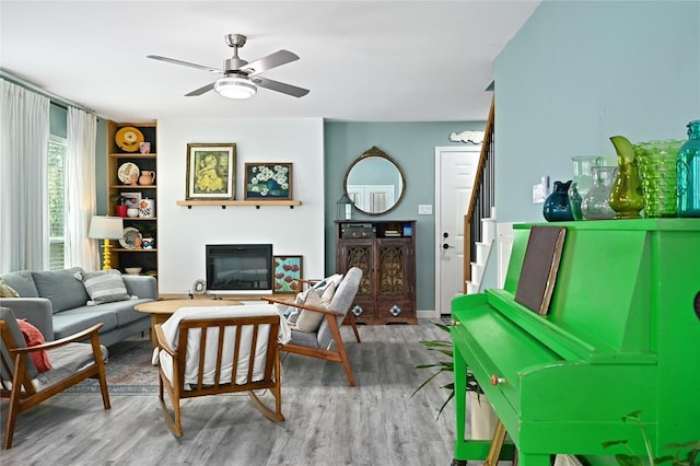 living room featuring stairs, a ceiling fan, a glass covered fireplace, and wood finished floors
