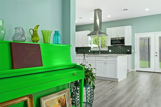 kitchen featuring island range hood, white cabinets, stainless steel microwave, and visible vents