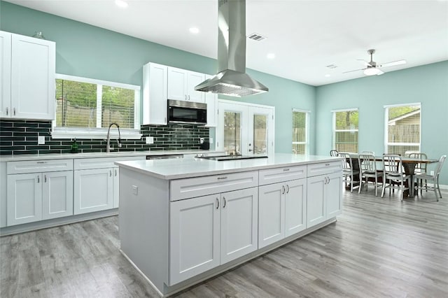 kitchen featuring a ceiling fan, a kitchen island, island range hood, a sink, and stainless steel microwave