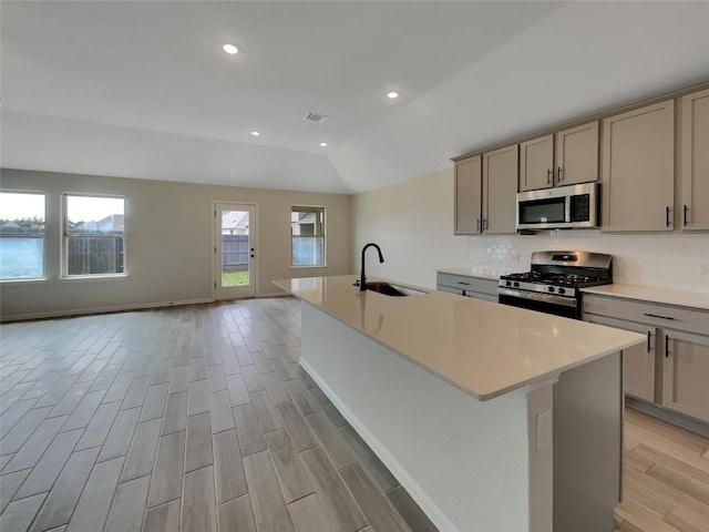 137 Periwinkle Ln, Bastrop, TX 78602 - kitchen featuring stainless steel appliances, a center island with sink, light wood finished floors, tasteful backsplash, and light countertops