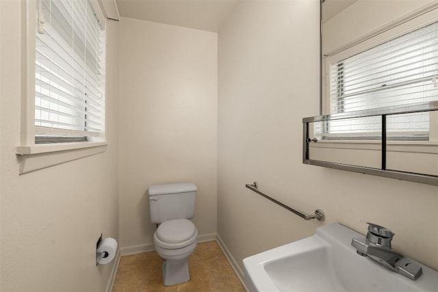 bathroom featuring toilet, a sink, baseboards, and a wealth of natural light