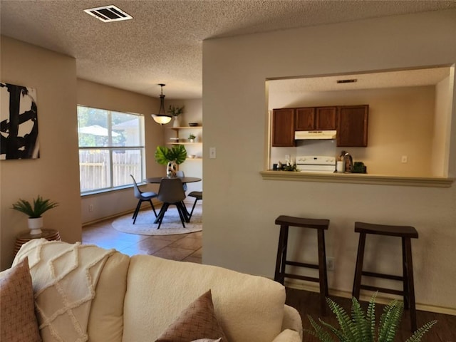 2516 Glen Field Dr, Cedar Park, TX 78613 - kitchen featuring range, under cabinet range hood, a kitchen breakfast bar, hanging light fixtures, and a textured ceiling