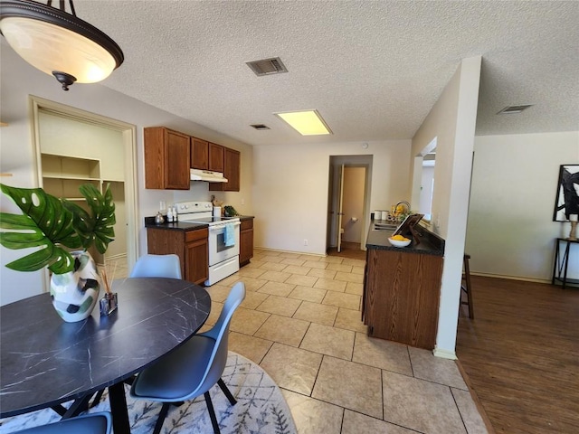 2516 Glen Field Dr, Cedar Park, TX 78613 - kitchen featuring white electric range oven, under cabinet range hood, dark countertops, brown cabinetry, and light tile patterned flooring