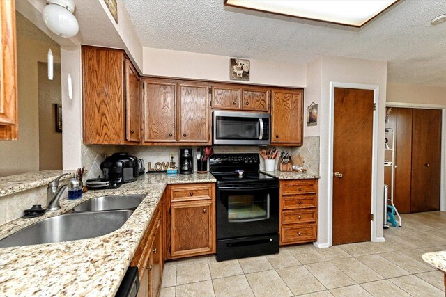 1306 Daytona Dr, Austin, TX 78733 - kitchen with stainless steel microwave, black range with electric cooktop, brown cabinetry, a textured ceiling, and light tile patterned floors