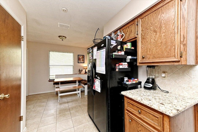 1306 Daytona Dr, Austin, TX 78733 - kitchen featuring black fridge, tasteful backsplash, brown cabinetry, light tile patterned flooring, and a textured ceiling